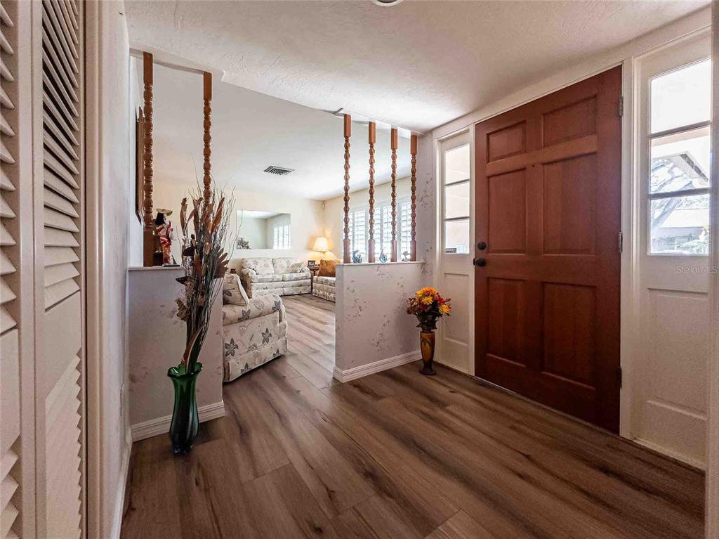 An entryway with wood-look flooring, a wooden front door, and a partial room divider — 1830 OAK FOREST DRIVE S, CLEARWATER, FL