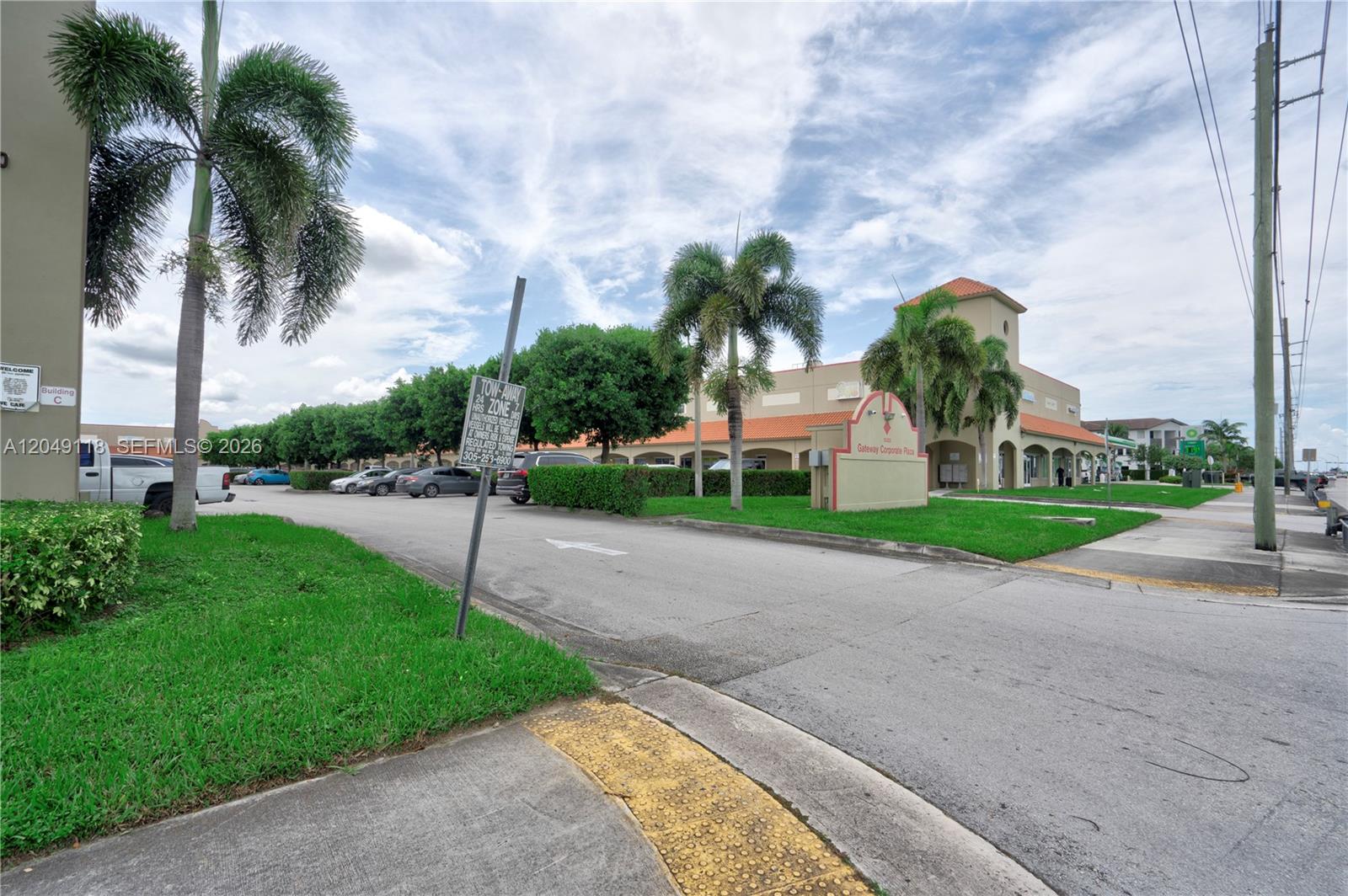 An exterior view of a commercial plaza with palm trees, parking, and a signage monument — 15420 SW 136th St # 6, Miami FL 33196, MIAMI, FL