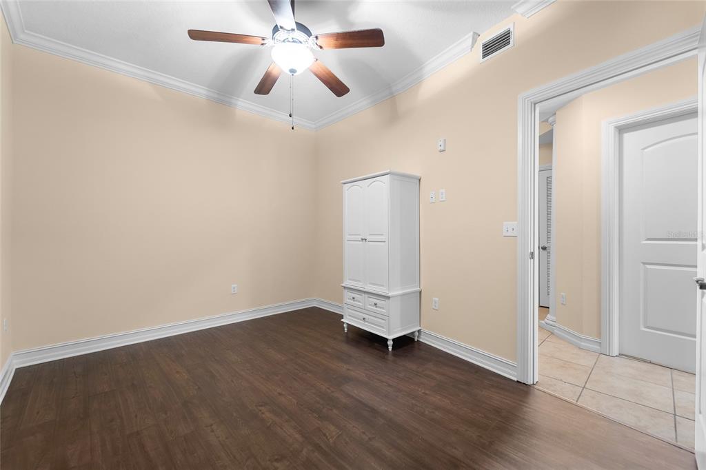An empty room features dark wood flooring, beige walls, a ceiling fan, and a white armoire — 13941 CLUBHOUSE DRIVE UNIT 106, TAMPA, FL