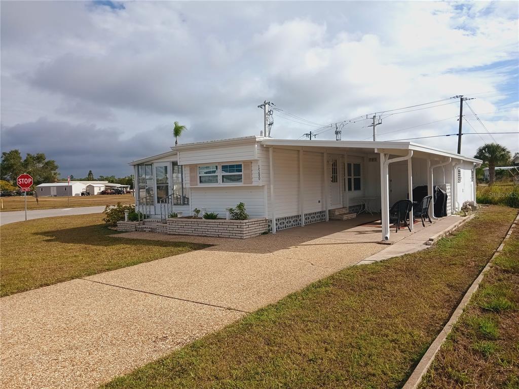 A white mobile home with a carport and a concrete driveway under a cloudy sky — 1580 BLIND BROOK DRIVE, SARASOTA, FL