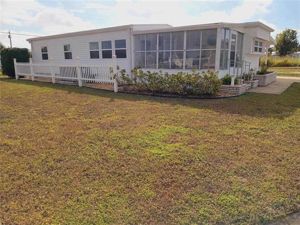 A white manufactured home features a screened-in porch, a white picket fence, and landscaping — 1580 BLIND BROOK DRIVE, SARASOTA, FL