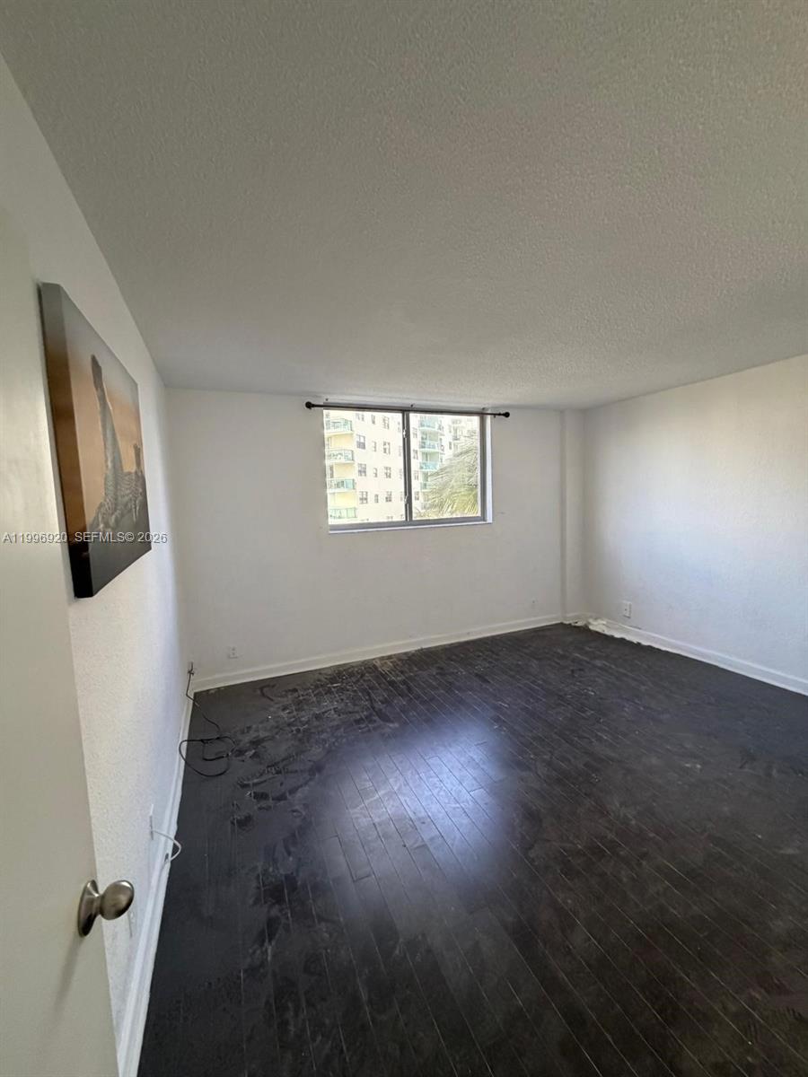 An empty room features dark wood flooring, white walls, and a single window — 4001 S Ocean Dr # 4H, Hollywood FL 33019, HOLLYWOOD, FL