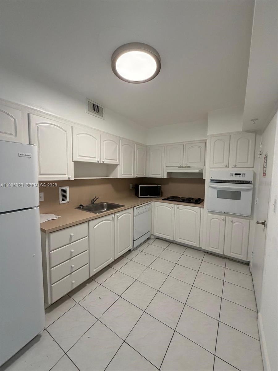 A kitchen features white cabinets, a white refrigerator, a built-in oven, and tiled flooring — 4001 S Ocean Dr # 4H, Hollywood FL 33019, HOLLYWOOD, FL