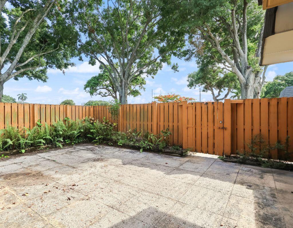 A paved patio area enclosed by a wooden fence with mature trees in the background — 2229 22nd Way, West Palm Beach FL 33407, WEST PALM BEACH, FL