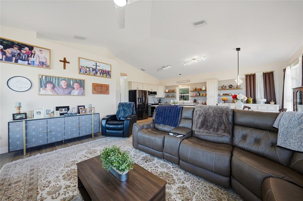 A living room features a brown sectional sofa, a patterned rug, and a kitchen background — 2481 NE FAYE TERRACE, ARCADIA, FL