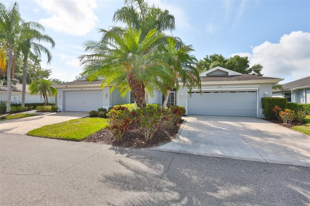 A single-story duplex with two garages, a paved driveway, and palm trees in the front yard — 951 VILLEROY GREENS DRIVE, SUN CITY CENTER, FL