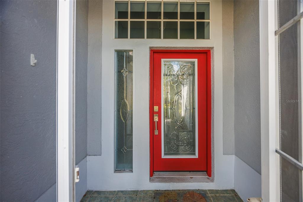 A bright red front door with a glass insert and sidelight sits under a transom window — 951 VILLEROY GREENS DRIVE, SUN CITY CENTER, FL