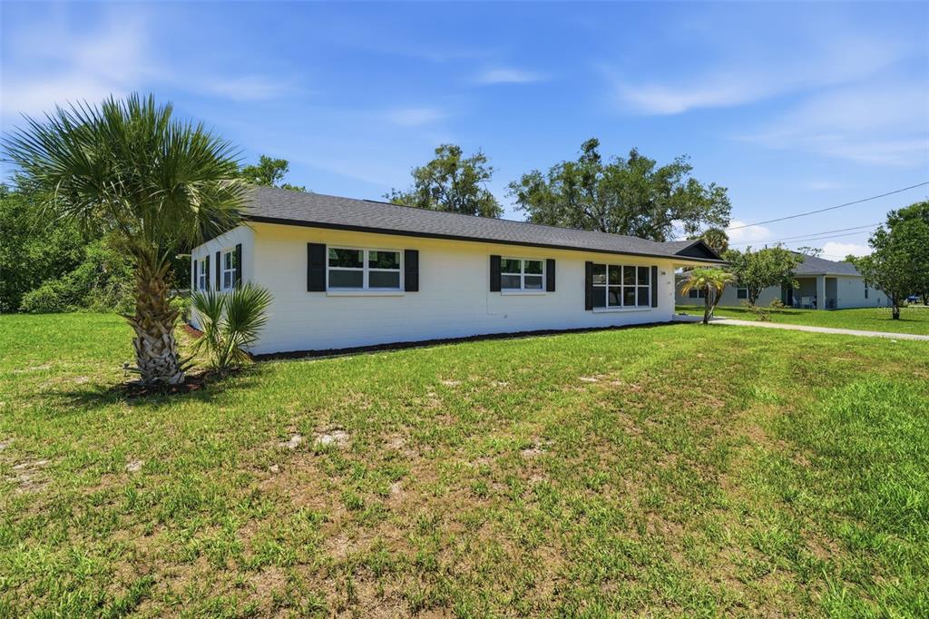 A single-story white house with black shutters sits on a grassy lot with palm trees — 206 MARGARITA ROAD, DEBARY, FL
