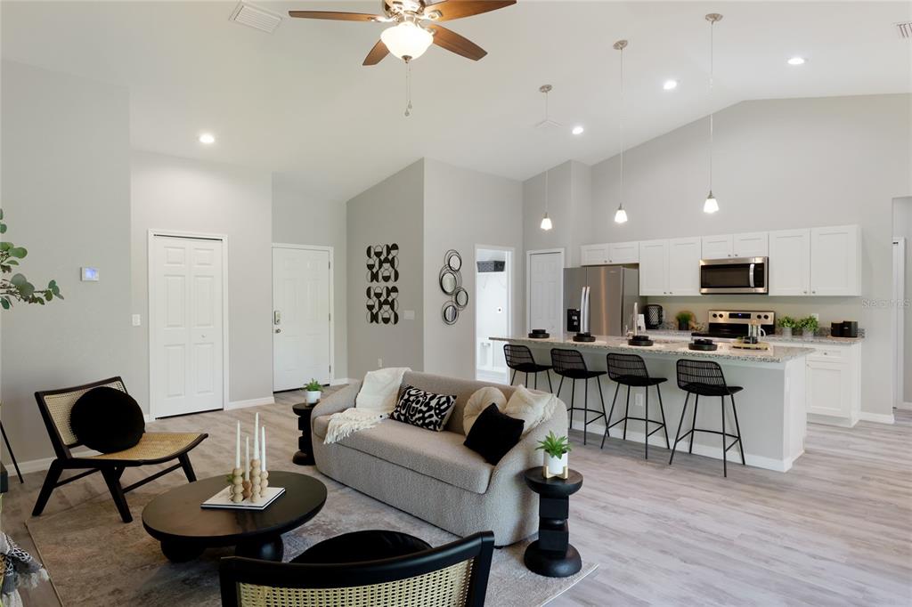An open-concept living room and kitchen featuring light wood floors, white cabinetry, and neutral furniture — 4450 WALL LANE, NORTH PORT, FL