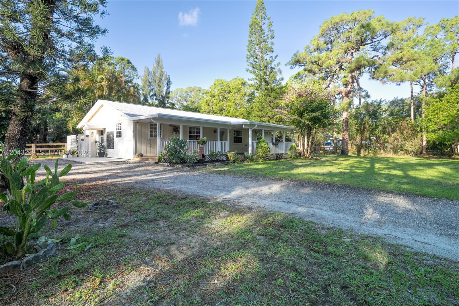 A single-story house with a white porch sits on a gravel driveway near trees — 15160 Scotts Pl, Loxahatchee FL 33470, LOXAHATCHEE, FL