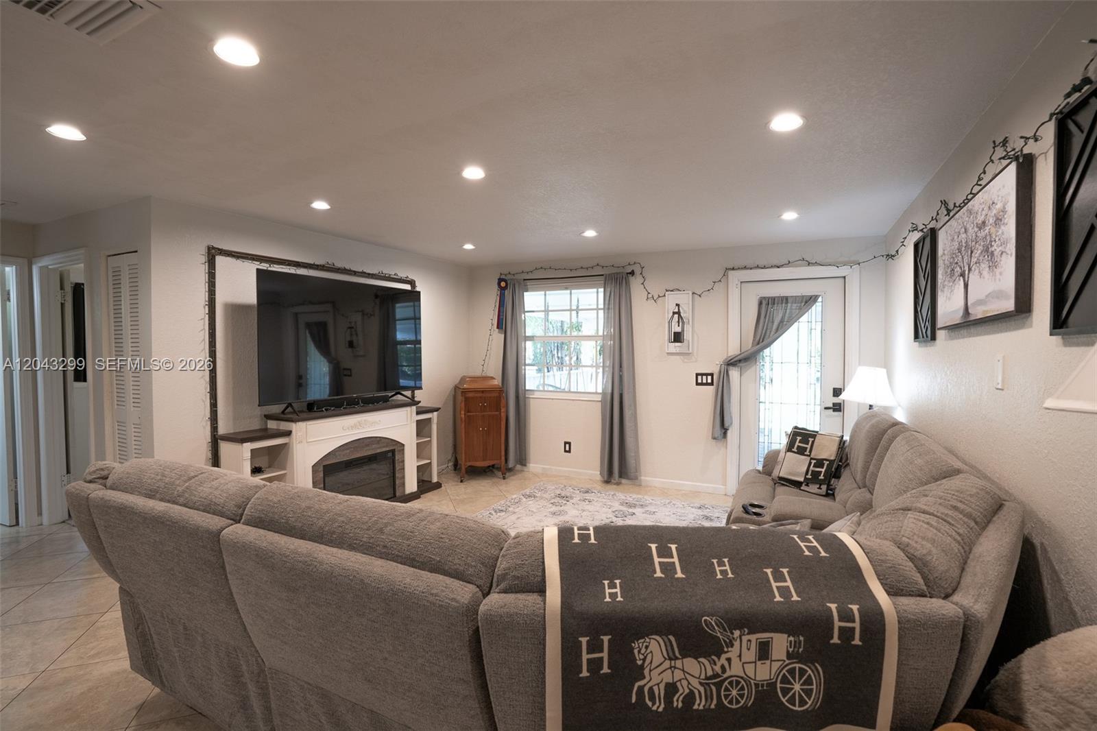A living room features a large gray sectional sofa, a fireplace media console, and recessed lighting — 15160 Scotts Pl, Loxahatchee FL 33470, LOXAHATCHEE, FL