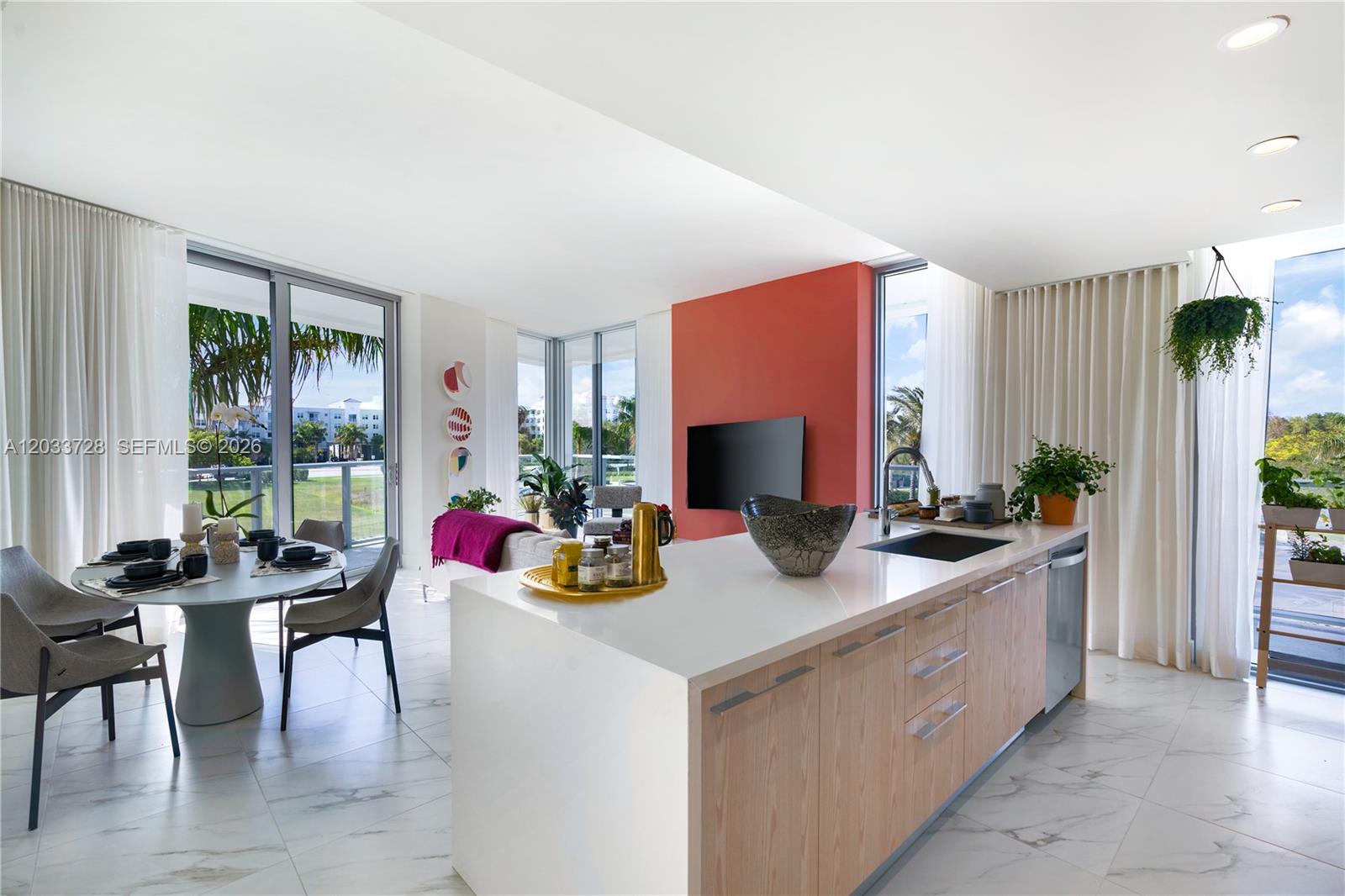 A modern open-concept kitchen and dining area features white marble floors and a red accent wall — 2000 Metropica Way # 203, Sunrise FL 33323, SUNRISE, FL