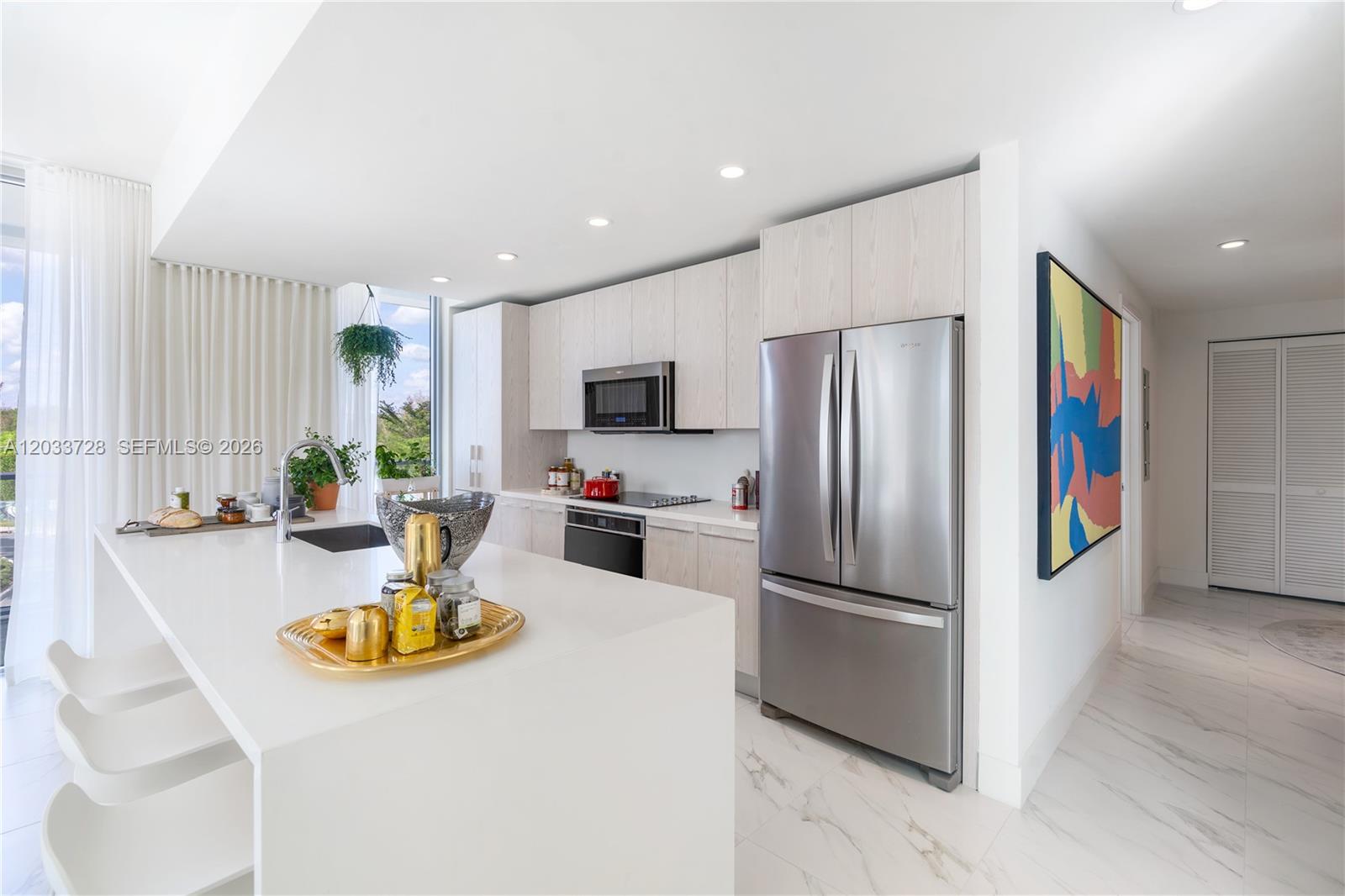 A modern kitchen features light wood cabinetry, white countertops, stainless steel appliances, and marble flooring — 2000 Metropica Way # 203, Sunrise FL 33323, SUNRISE, FL