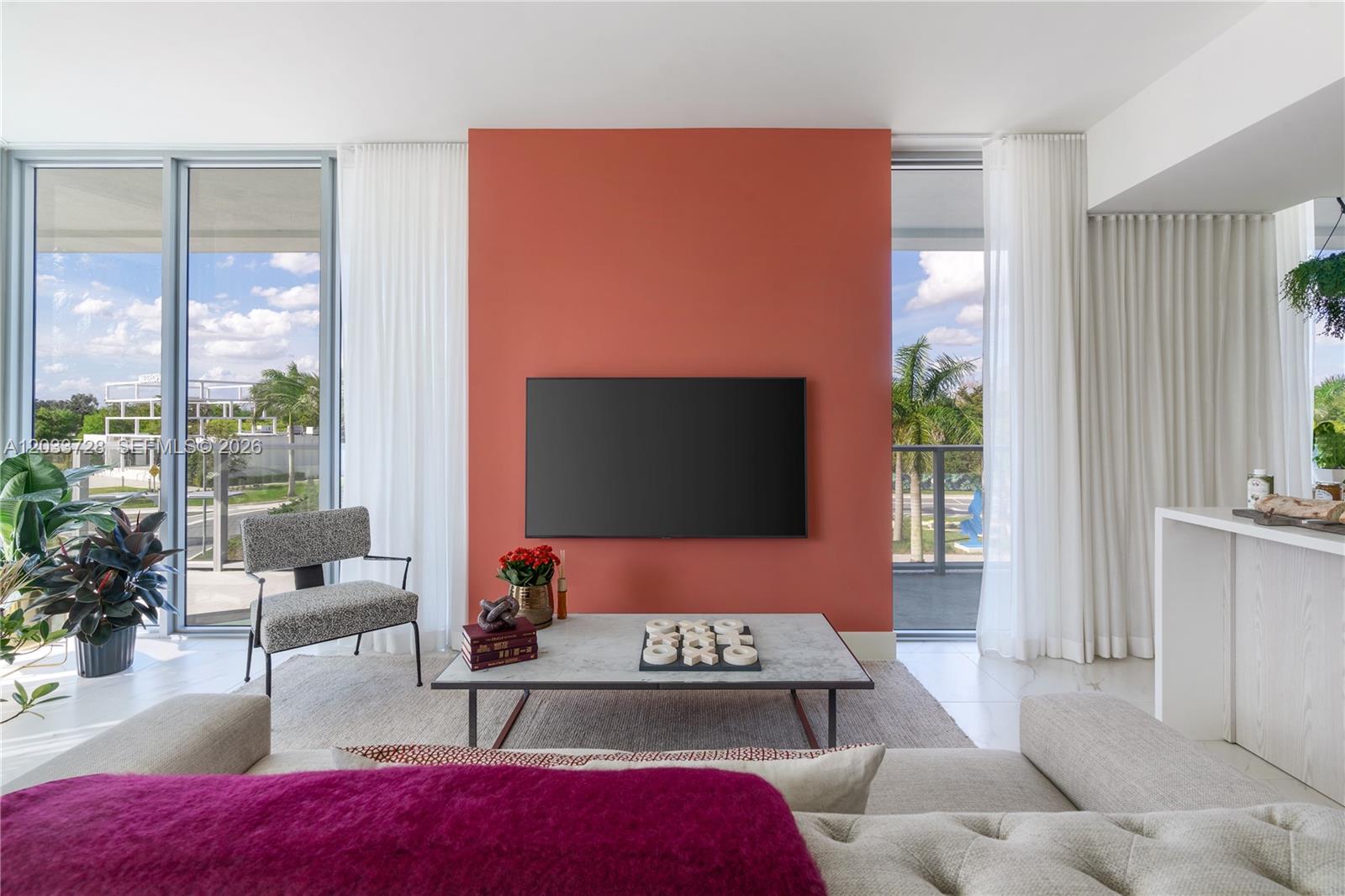 A living room features a coral accent wall with a mounted television and floor-to-ceiling windows — 2000 Metropica Way # 203, Sunrise FL 33323, SUNRISE, FL
