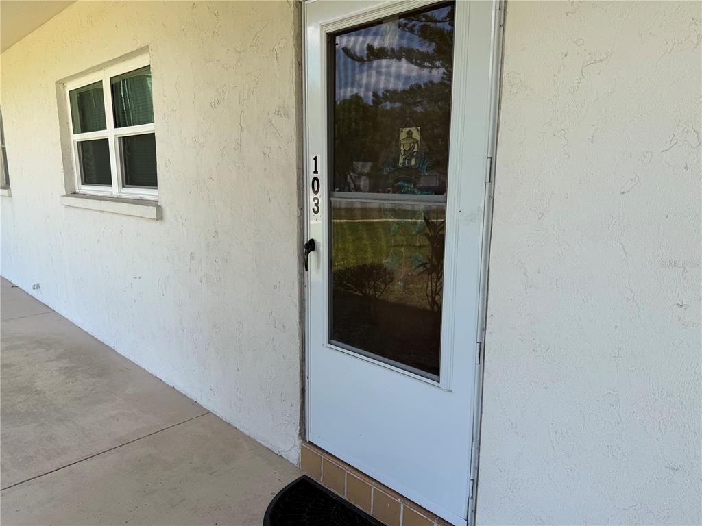 A white exterior door labeled 103 sits beside a window on a concrete walkway — 245 CENTER ROAD UNIT 103, VENICE, FL
