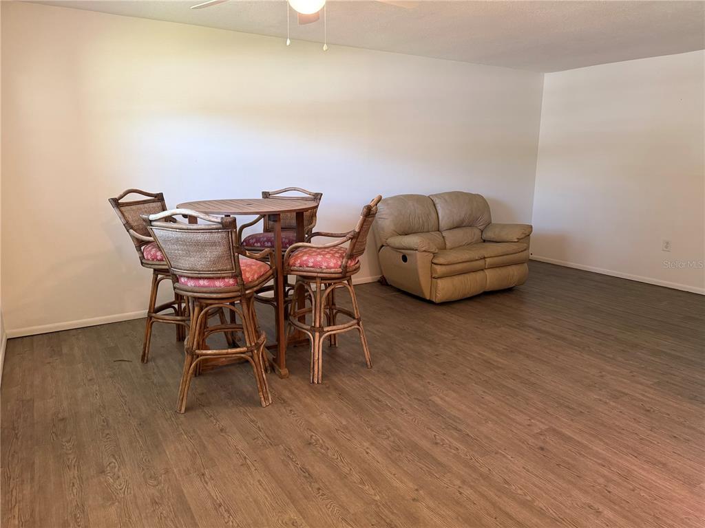 A room with wood-look flooring features a round dining table with four chairs and a loveseat — 245 CENTER ROAD UNIT 103, VENICE, FL