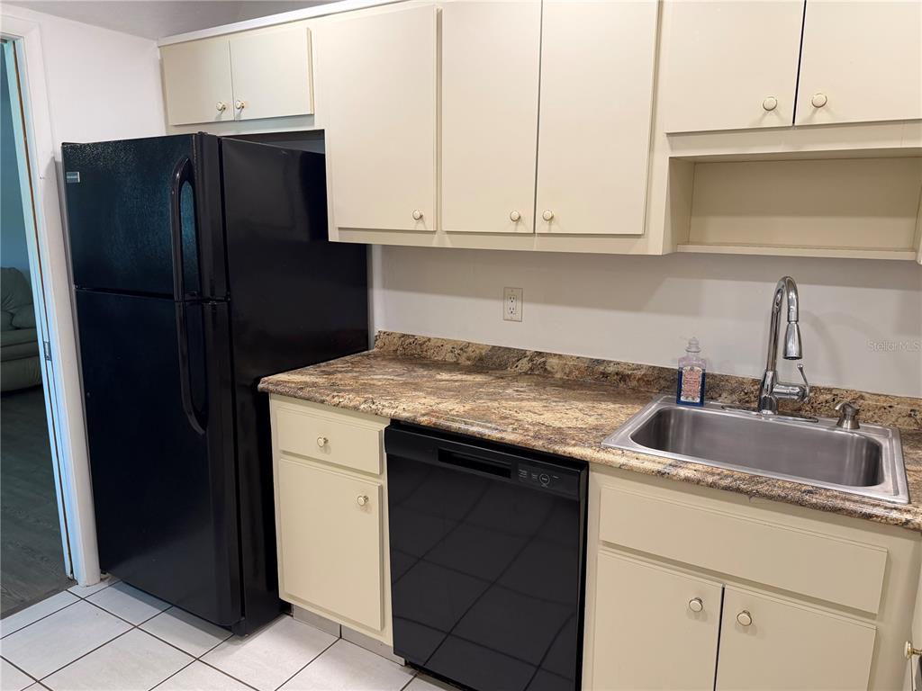 A kitchen features light-colored cabinets, a black refrigerator and dishwasher, and a granite countertop — 245 CENTER ROAD UNIT 103, VENICE, FL
