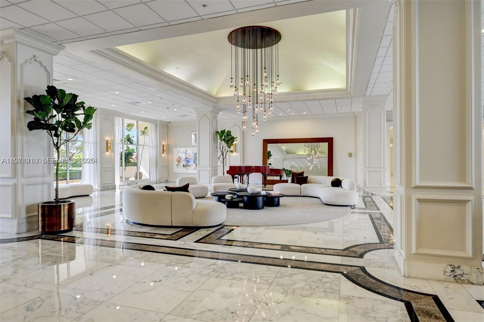 A spacious lobby features marble floors, a large chandelier, curved white sofas, and a piano — 5600 Collins Ave # 7Y, Miami Beach FL 33140, MIAMI BEACH, FL