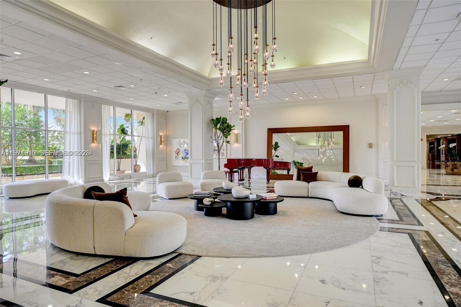 A spacious, white-tiled lobby features a large circular rug, curved sofas, and a grand chandelier — 5600 Collins Ave # 7Y, Miami Beach FL 33140, MIAMI BEACH, FL