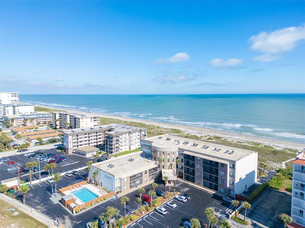 An aerial view shows a multi-story beachfront apartment complex with a pool and parking lot — 333 N ATLANTIC AVENUE UNIT 305, COCOA BEACH, FL