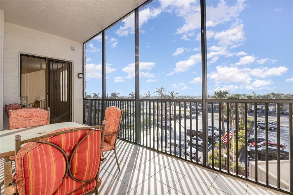 A screened-in balcony features tiled flooring, patio furniture, and a view of a parking lot — 333 N ATLANTIC AVENUE UNIT 305, COCOA BEACH, FL