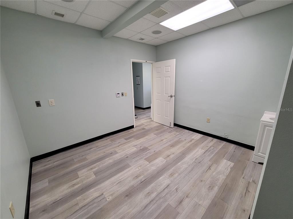 An empty office room features light gray walls, wood-look vinyl flooring, and a white door — 37310 PURE WATER WAY, ZEPHYRHILLS, FL