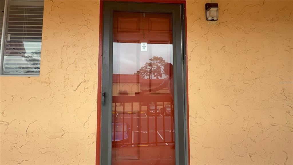A glass storm door is mounted on a textured, light orange exterior wall — 2800 N POWERS DRIVE UNIT 9, ORLANDO, FL