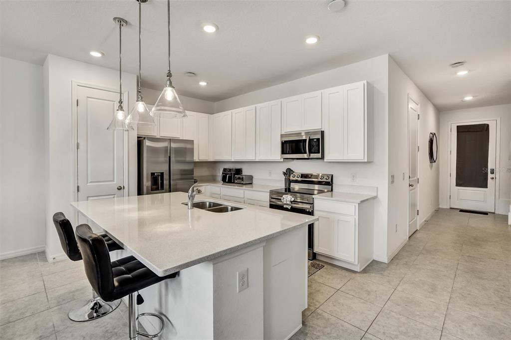 A modern kitchen features white cabinets, a quartz island with seating, and stainless steel appliances — 1056 PLANTATION LANE, DAVENPORT, FL