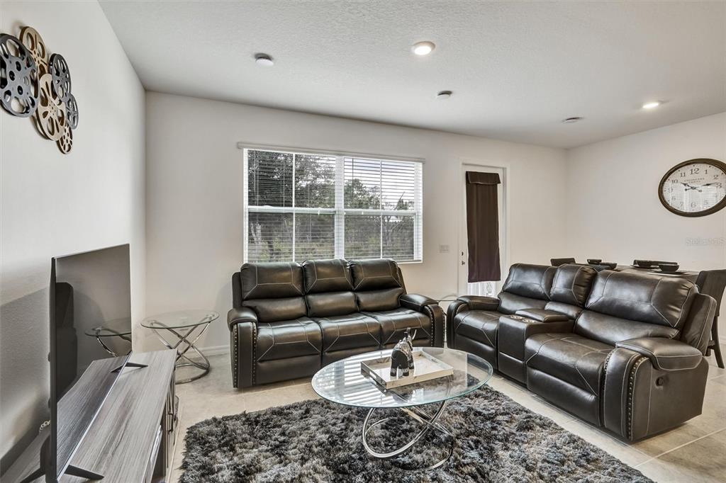 A living room features dark leather reclining sofas, a glass coffee table, and a wall clock — 1056 PLANTATION LANE, DAVENPORT, FL