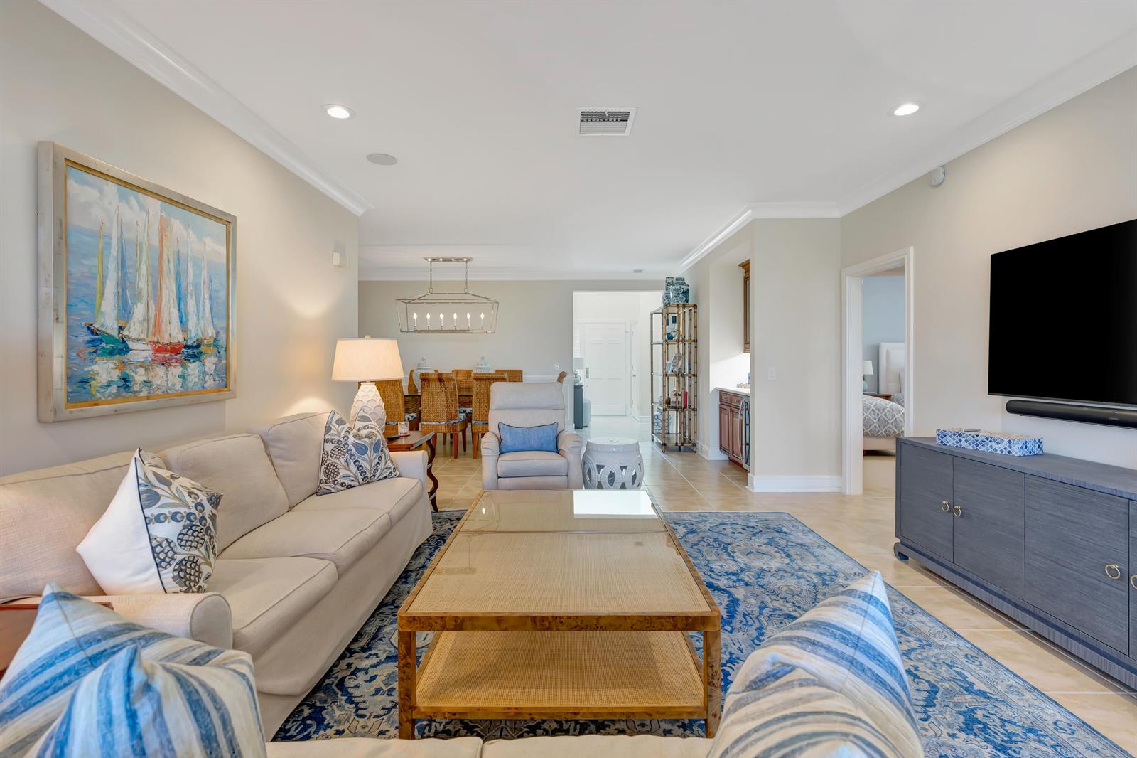 A living room features a beige sofa, blue patterned rug, glass coffee table, and television — 1201 Captains Way, Jupiter FL 33477, JUPITER, FL