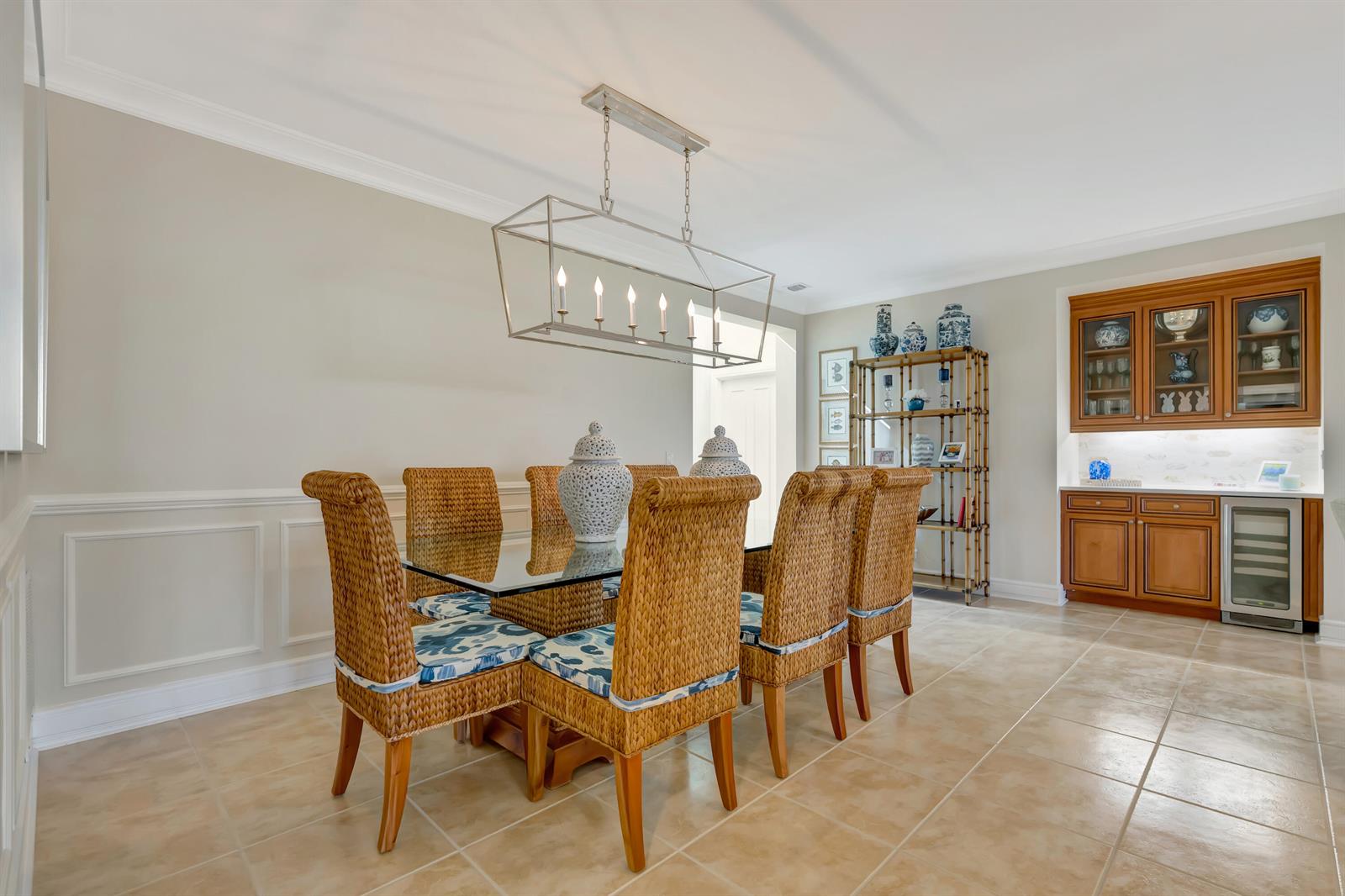 A dining room features a glass-top table with wicker chairs, a metal chandelier, and cabinetry — 1201 Captains Way, Jupiter FL 33477, JUPITER, FL