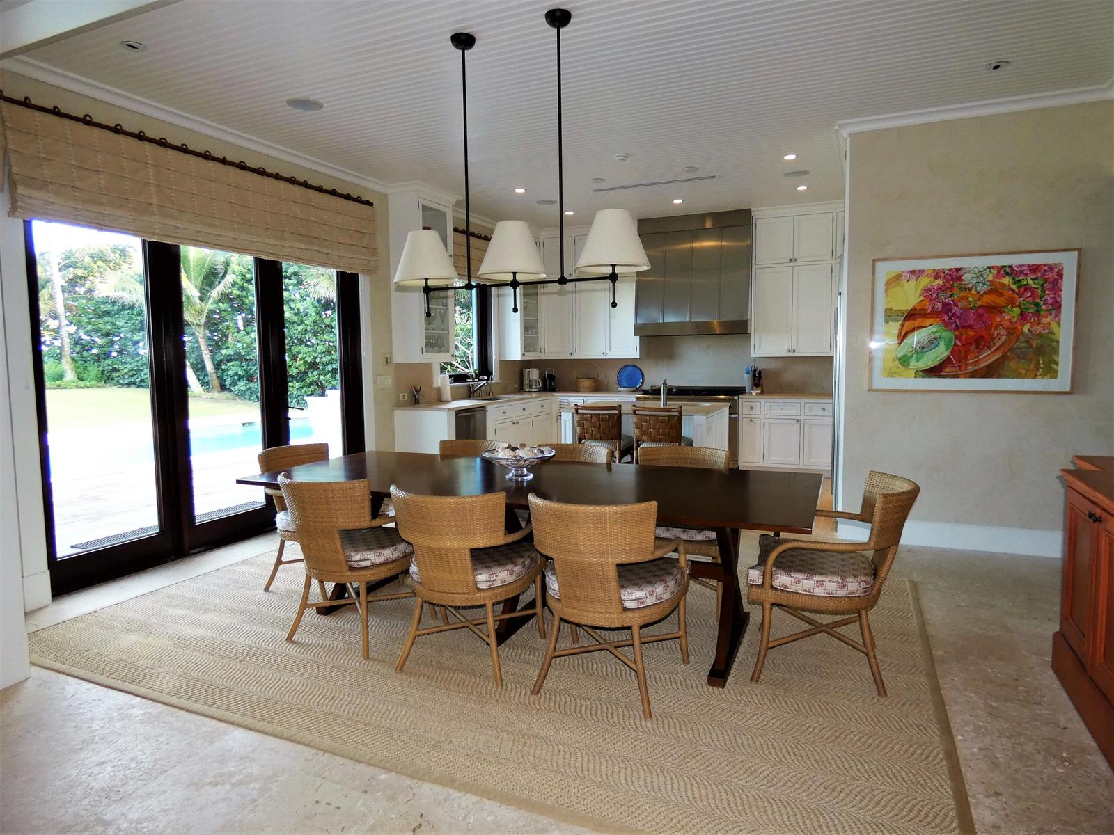A dining area with a wooden table and wicker chairs sits before an open kitchen — 521 S Beach Road, Jupiter Island FL 33455, JUPITER ISLAND, FL