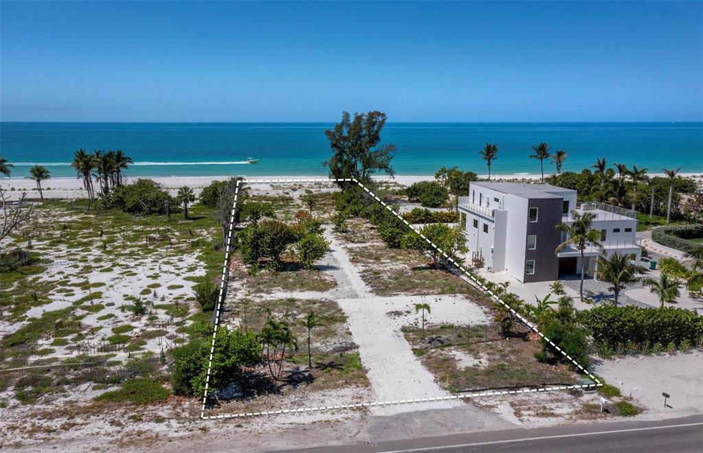 An aerial view shows a vacant beachfront lot outlined in white next to a modern house — 6351 GULF OF MEXICO DRIVE, LONGBOAT KEY, FL