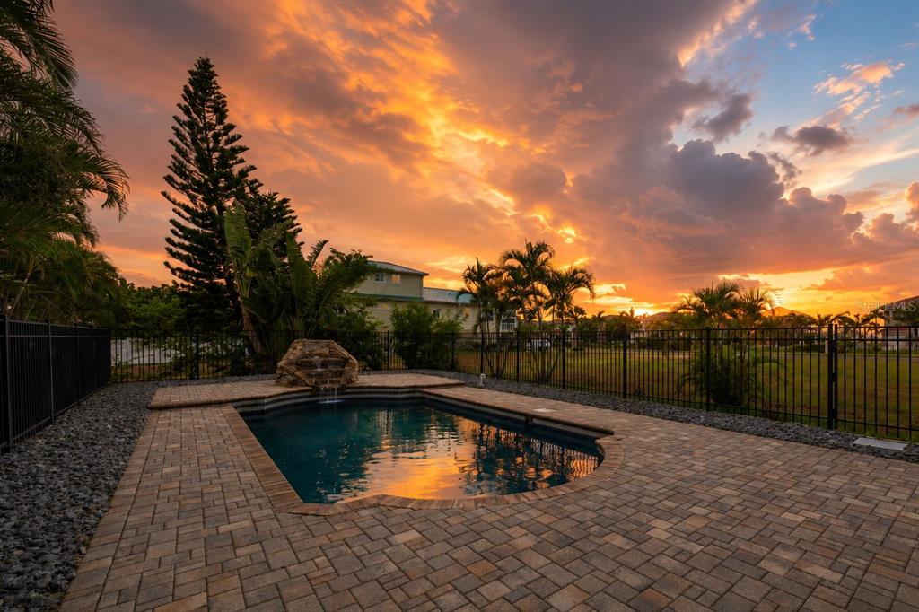 A backyard swimming pool with a stone water feature sits on a paved patio at sunset — 1340 APOLLO BEACH BOULEVARD S, APOLLO BEACH, FL
