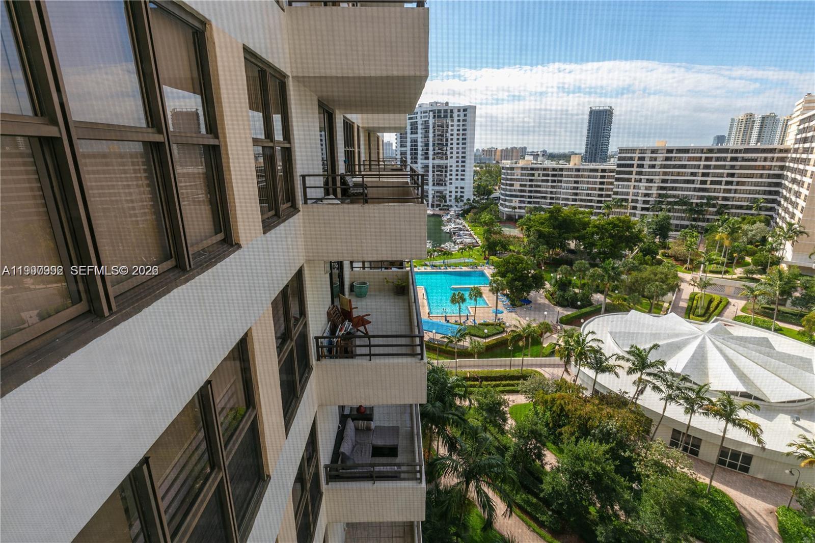 An elevated view shows apartment balconies overlooking a swimming pool, landscaped grounds, and city buildings — 2500 PARKVIEW DR # 1418, Hallandale Beach FL 33009, HALLANDALE BEACH, FL