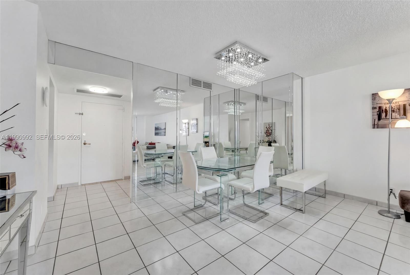A dining area features a glass table, white chairs, a crystal chandelier, and mirrored walls — 2500 PARKVIEW DR # 1418, Hallandale Beach FL 33009, HALLANDALE BEACH, FL