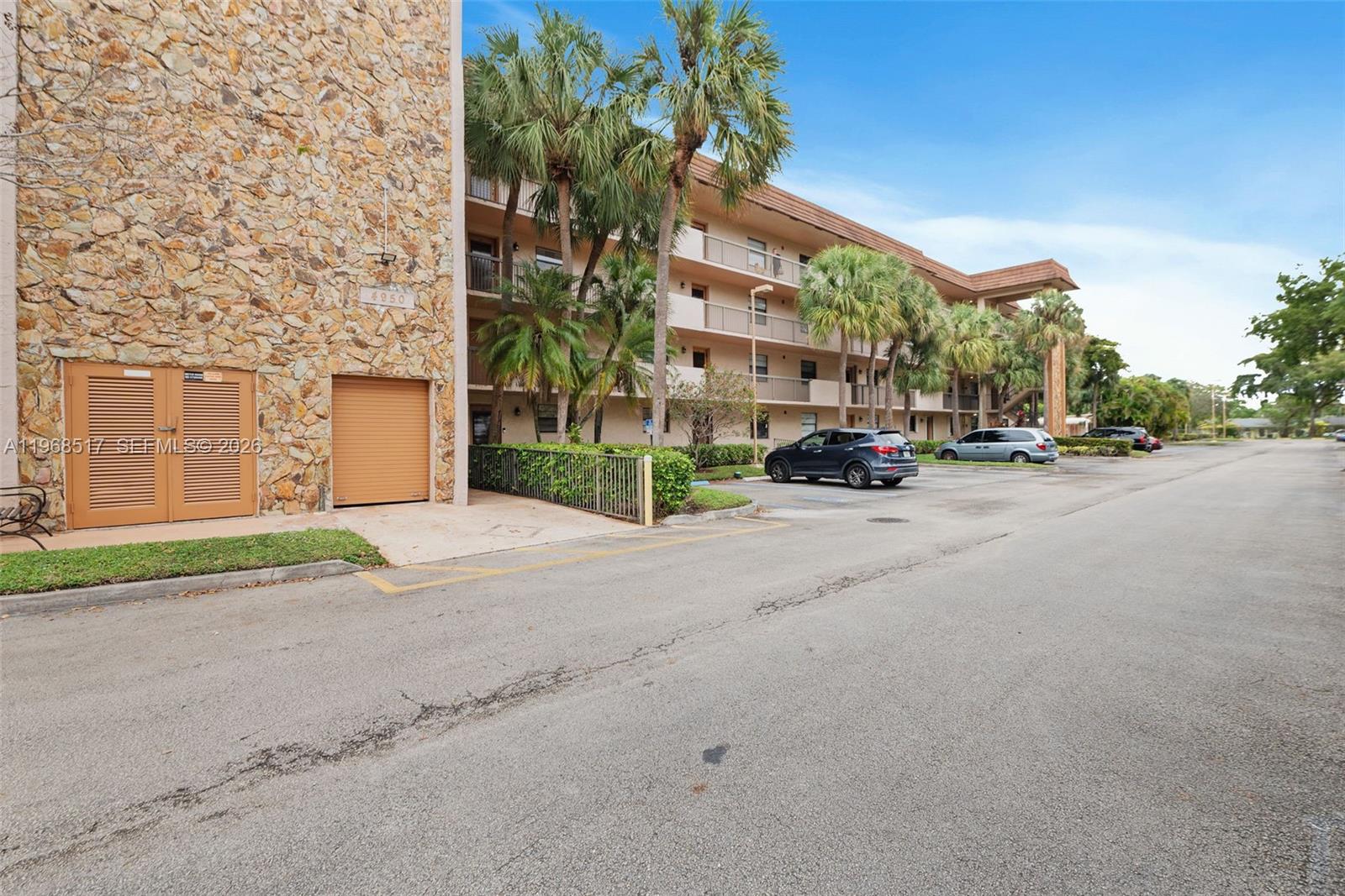 An exterior view shows a multi-story apartment building with a stone facade and parking lot — 4950 E Sabal Palm Blvd # 310, Tamarac FL 33319, TAMARAC, FL