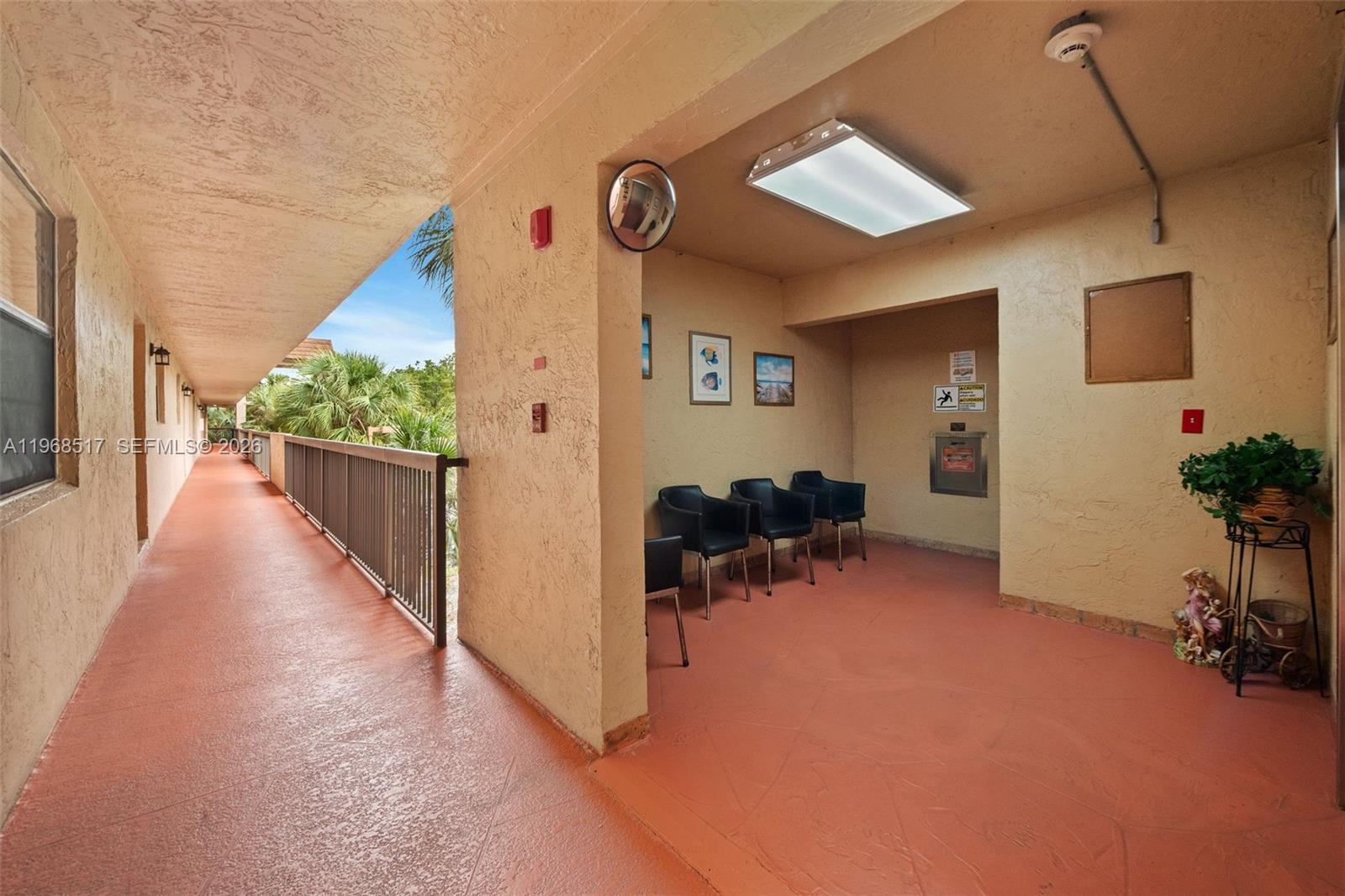 An outdoor apartment hallway features a seating area with chairs, a trash chute, and railings — 4950 E Sabal Palm Blvd # 310, Tamarac FL 33319, TAMARAC, FL