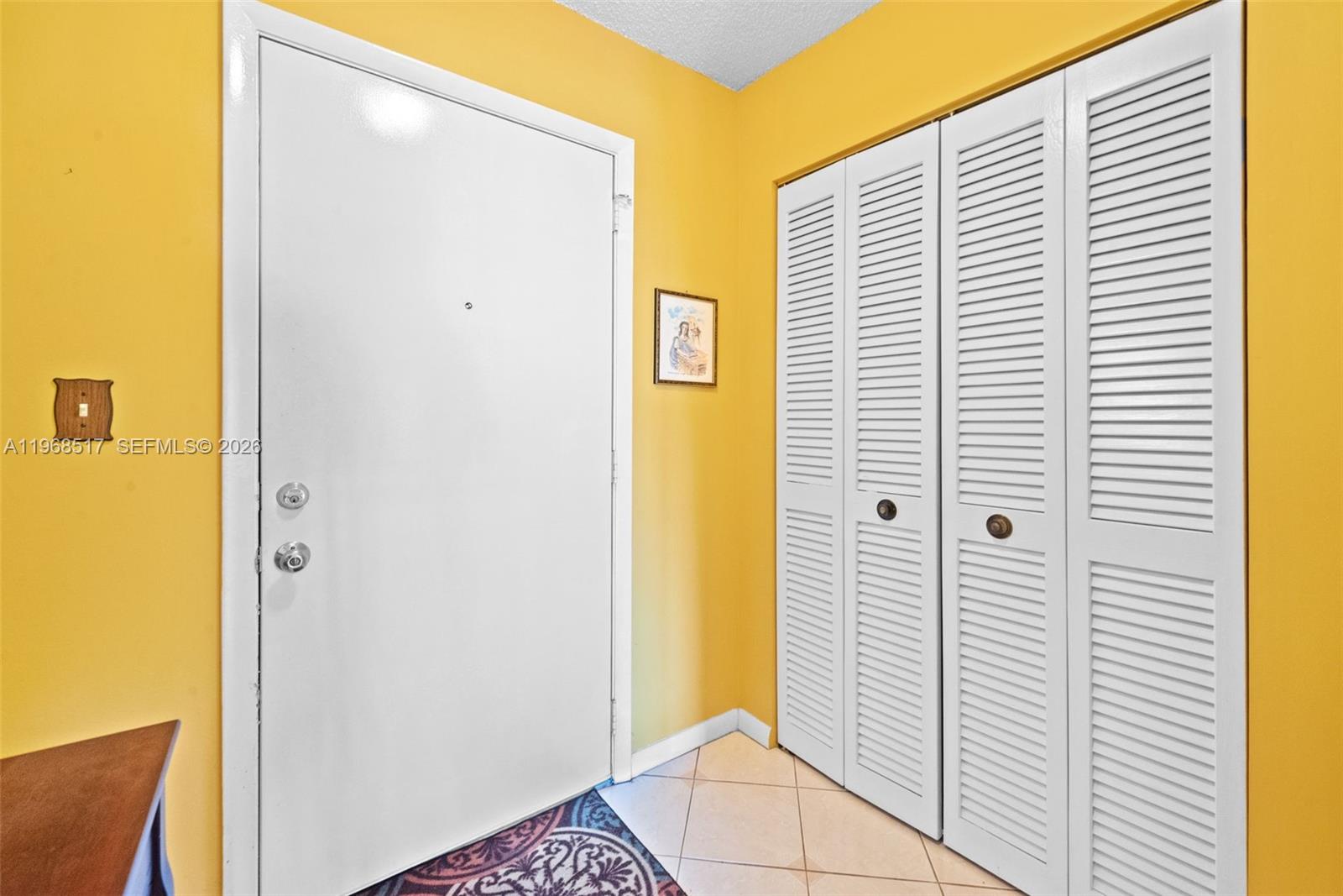 An entryway features a white door, louvered closet doors, and yellow walls — 4950 E Sabal Palm Blvd # 310, Tamarac FL 33319, TAMARAC, FL