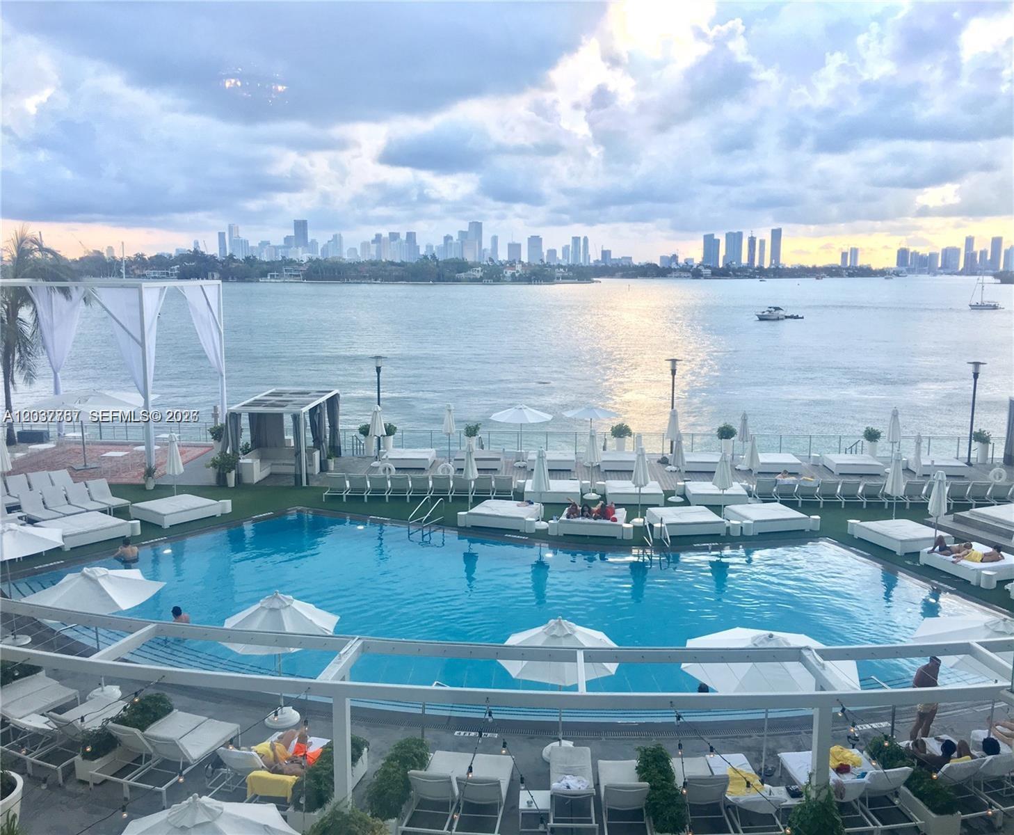 An outdoor swimming pool area features lounge chairs, umbrellas, and a view of the city skyline — 1100 West Ave # 525, Miami Beach FL 33139, MIAMI BEACH, FL