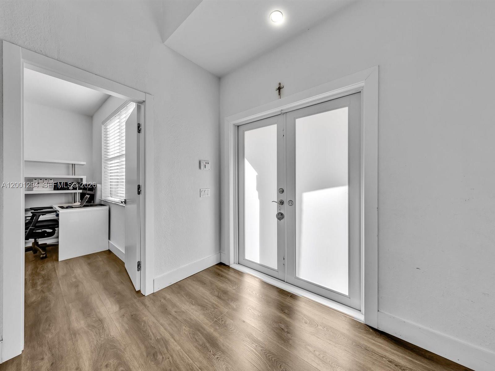 A room with wood-look flooring features a doorway leading to an office and double doors — 1042 Thistle Creek Ct, Weston FL 33327, WESTON, FL