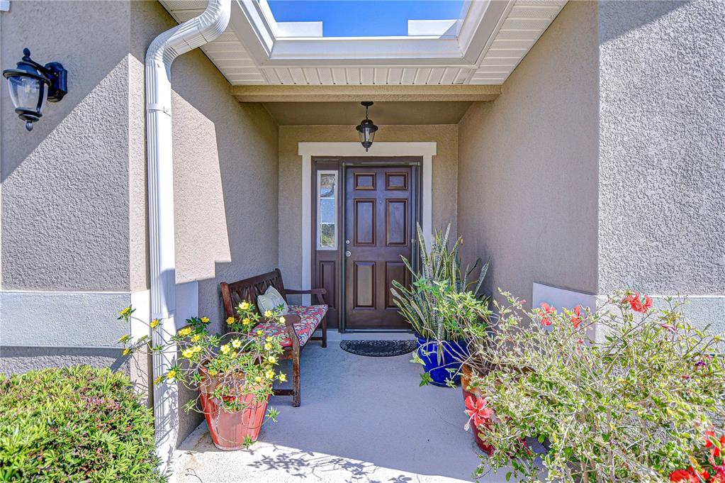 A covered entryway features a brown front door, a wooden bench, and potted plants — 6731 CASTLE GREEN PLACE, ZEPHYRHILLS, FL