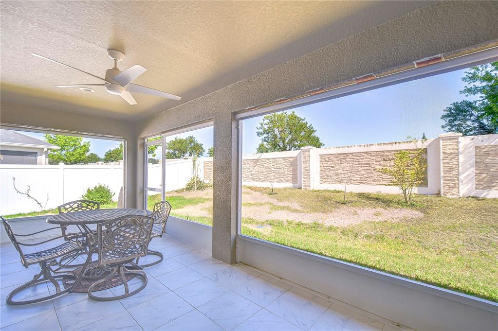 A covered patio with tiled flooring, a ceiling fan, and large screened windows overlooking a yard — 6731 CASTLE GREEN PLACE, ZEPHYRHILLS, FL