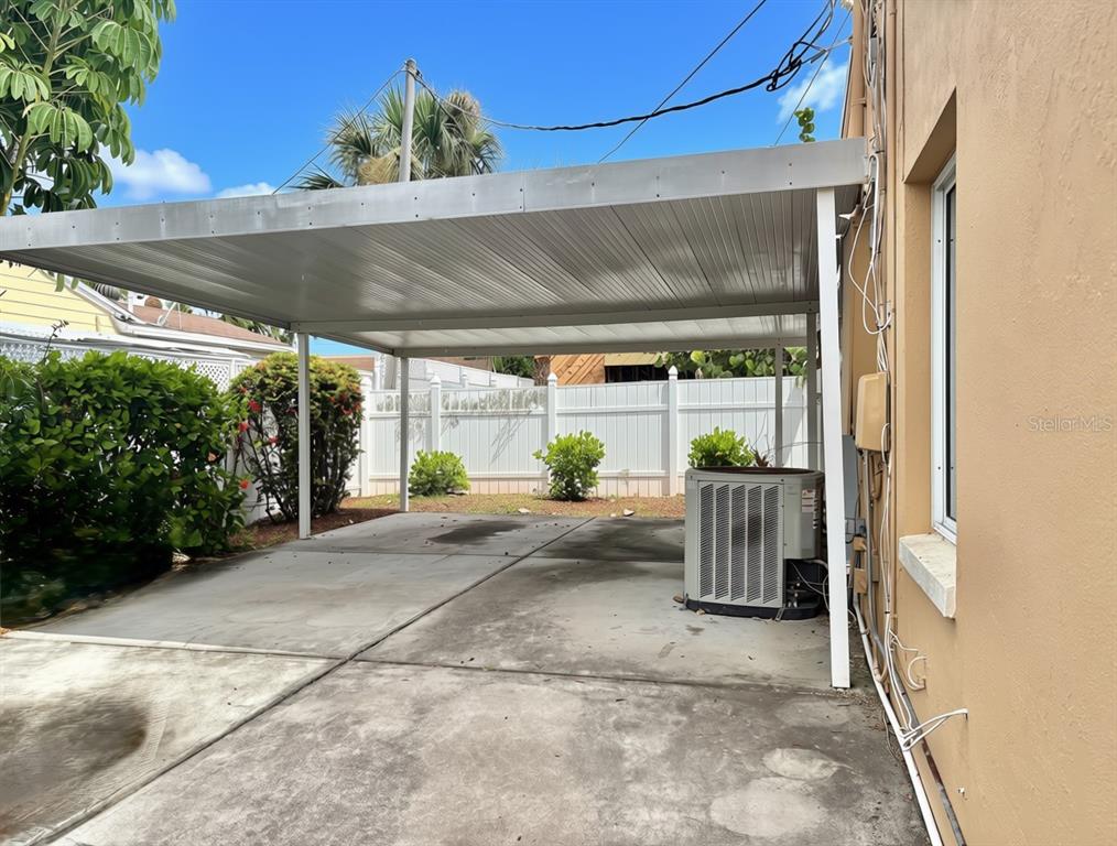 A concrete driveway features a metal carport cover next to an exterior wall and AC unit — 360 72ND AVENUE, ST PETERSBURG, FL