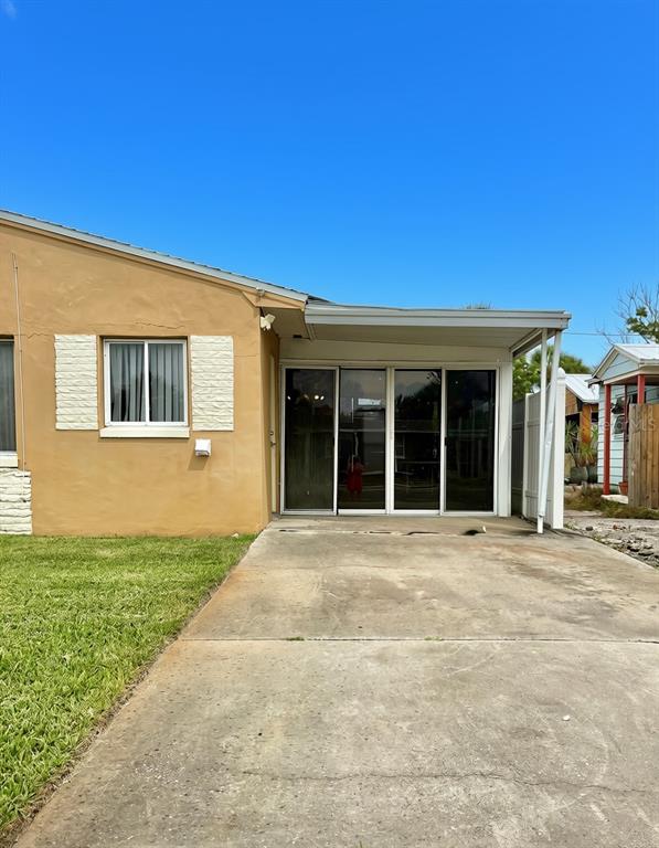 A tan house exterior features a concrete driveway, a covered patio, and sliding glass doors — 360 72ND AVENUE, ST PETERSBURG, FL