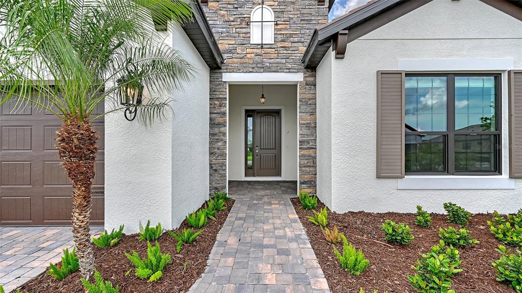 A stone-accented house exterior features a paved walkway leading to a dark brown front door — 204 TERACORSA DRIVE, NOKOMIS, FL