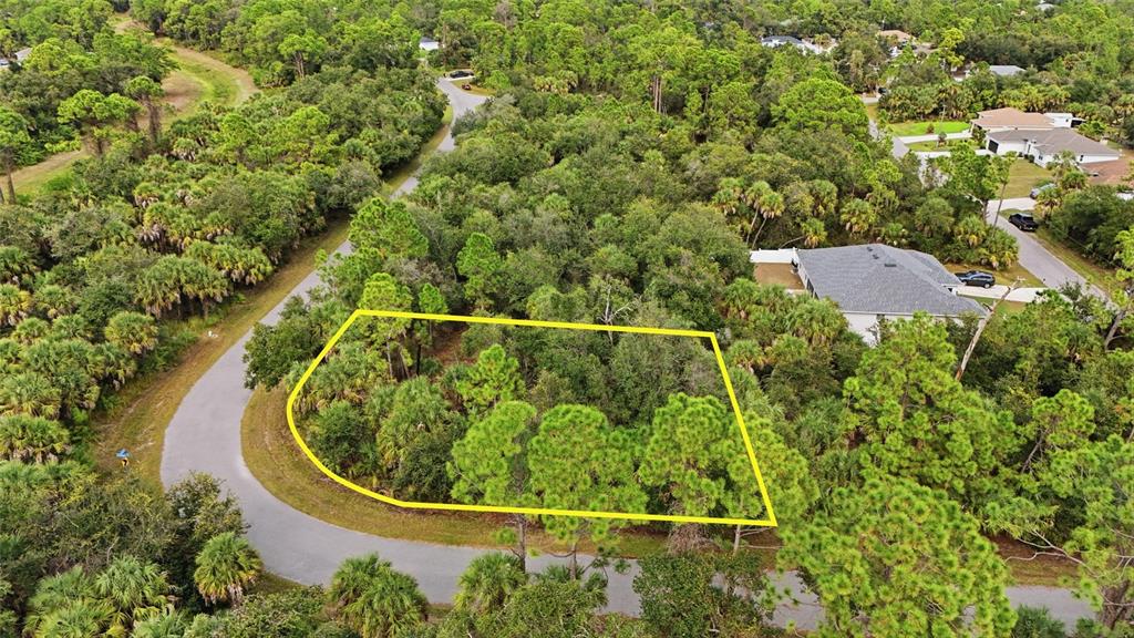 An aerial view shows a vacant, wooded residential lot outlined in yellow along a curved road — RAYFIELD DRIVE, NORTH PORT, FL