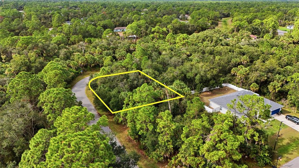 An aerial view shows a vacant, wooded residential lot outlined in yellow next to a house — RAYFIELD DRIVE, NORTH PORT, FL