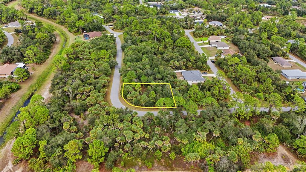 An aerial view shows a wooded, undeveloped residential lot outlined in yellow along a road — RAYFIELD DRIVE, NORTH PORT, FL