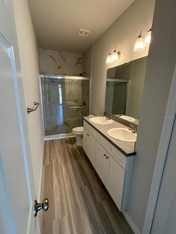 A bathroom with a double vanity, white cabinets, a walk-in shower, and wood-look flooring — 1462 LAS VILLAS BOULEVARD, SEBRING, FL